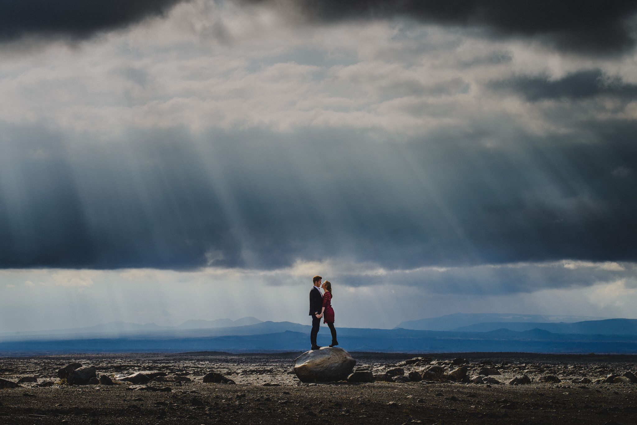 Romantic couple embracing on rugged icelandic rock under dramatic sunlight and stormy skies.