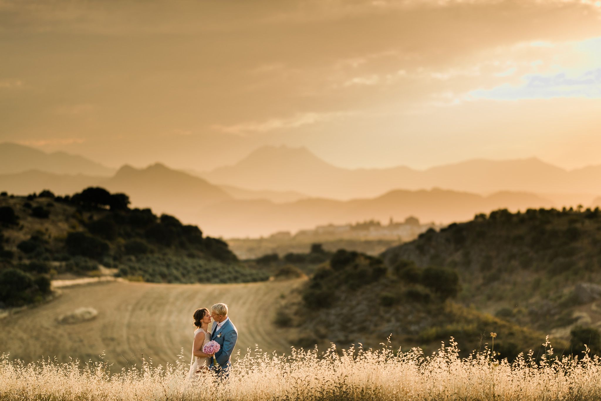 Romantic couple embracing in golden hour light amid rolling hills and distant mountains.