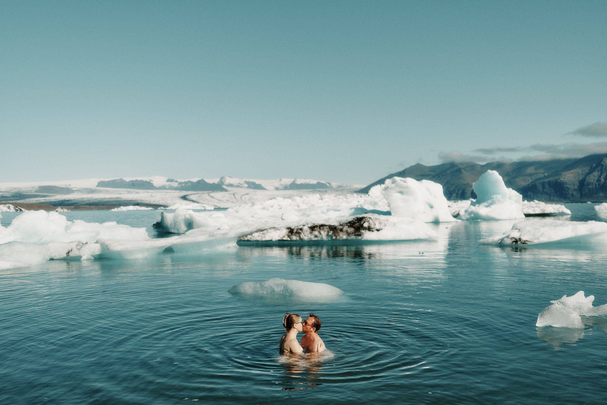 Couple kissing in icy glacial water with floating icebergs and snowy mountains in iceland.