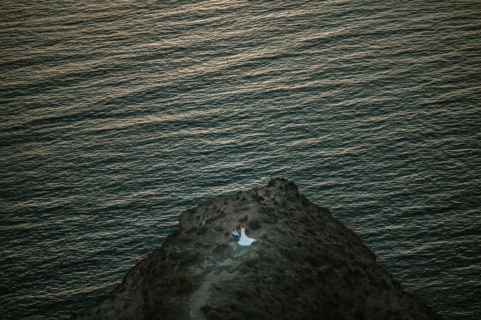 Aerial view of romantic couple embracing on rugged icelandic coastal cliff by the ocean.