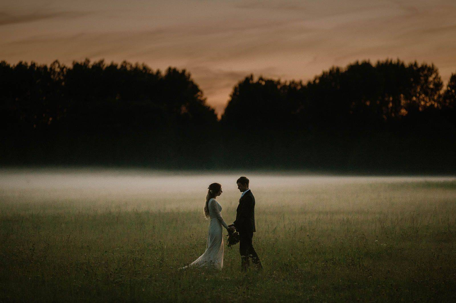 Romantic couple holding hands in misty sunset field with silhouetted trees, iceland wedding portrait.