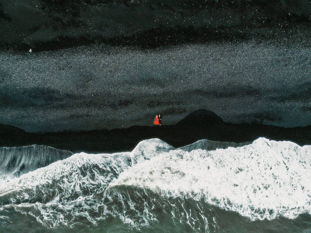 Bride in red on stormy iceland coast under starry night sky with crashing waves and mountains