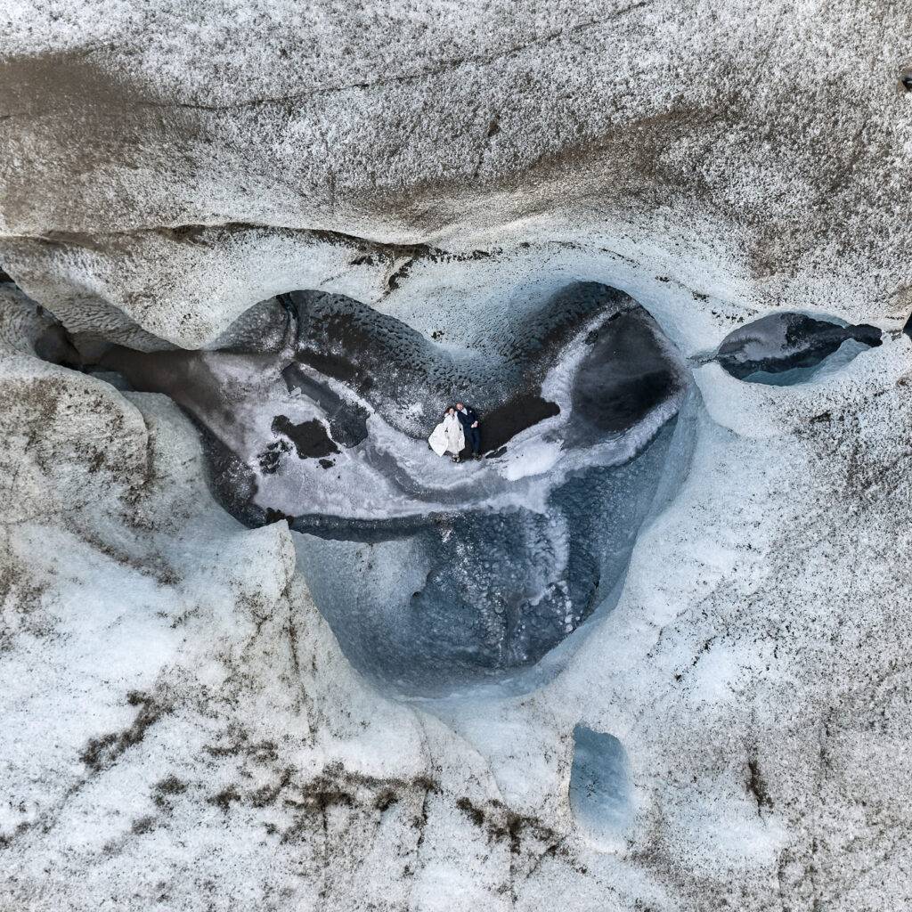 Romantic couple embraces in a stunning blue glacier ice hollow in iceland’s remote wilderness.