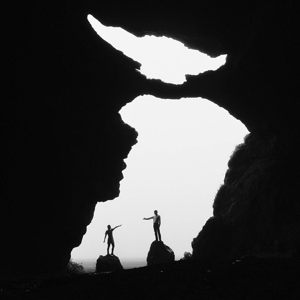 Silhouetted couple connecting inside jagged iceland cave with bright natural light outside.