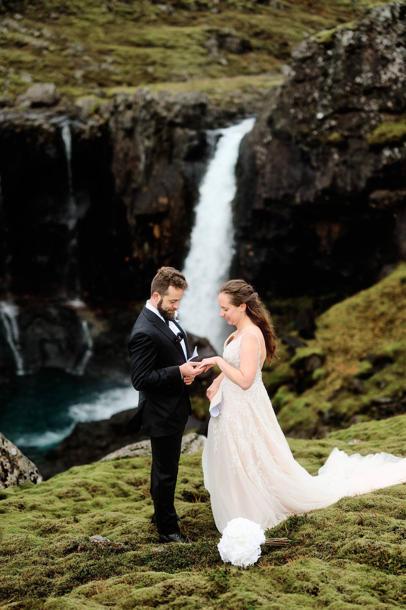 Bride and groom exchanging rings by a lush mossy landscape with icelandic waterfall backdrop.